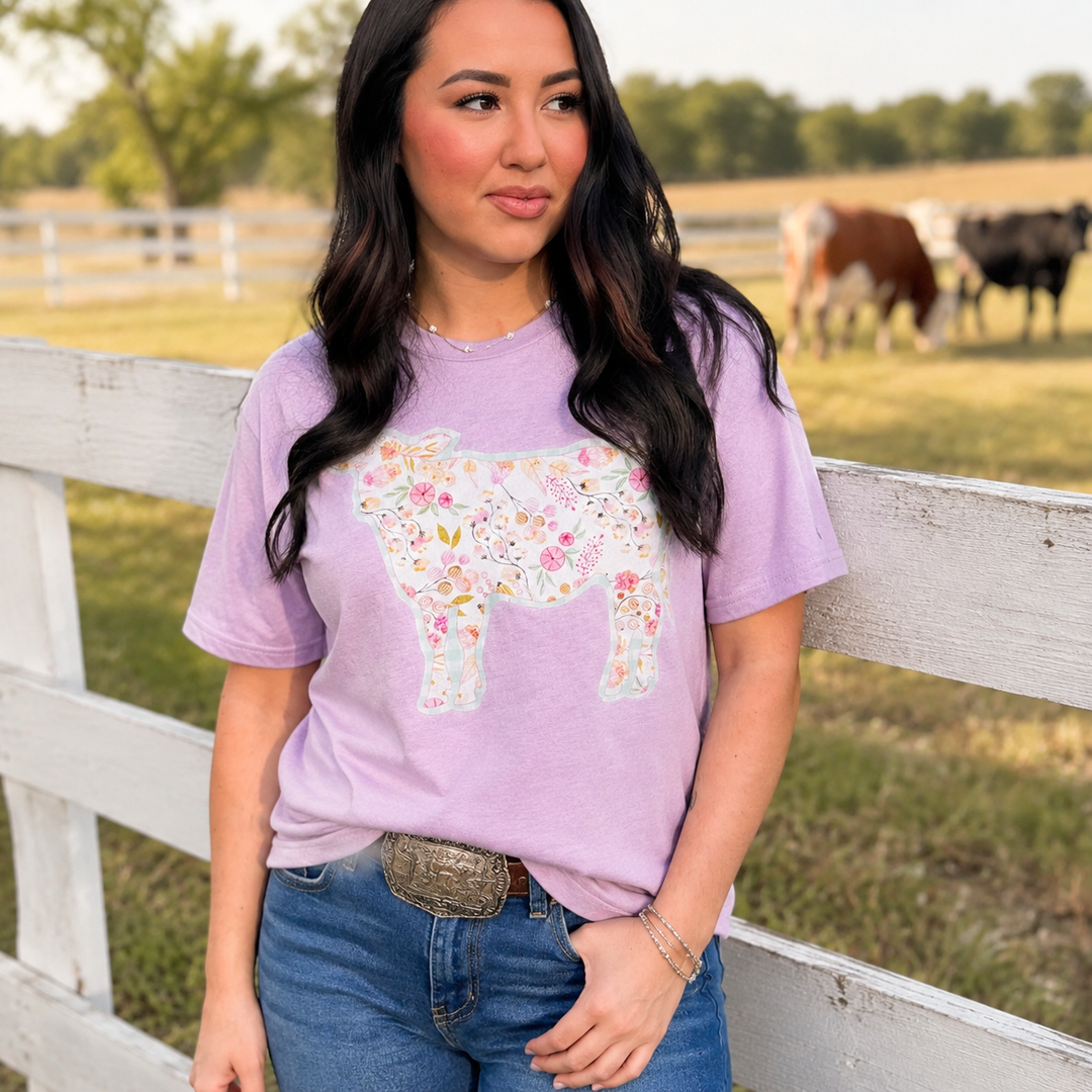 Woman wearing a lavender floral cow graphic T-shirt beside a white ranch fence