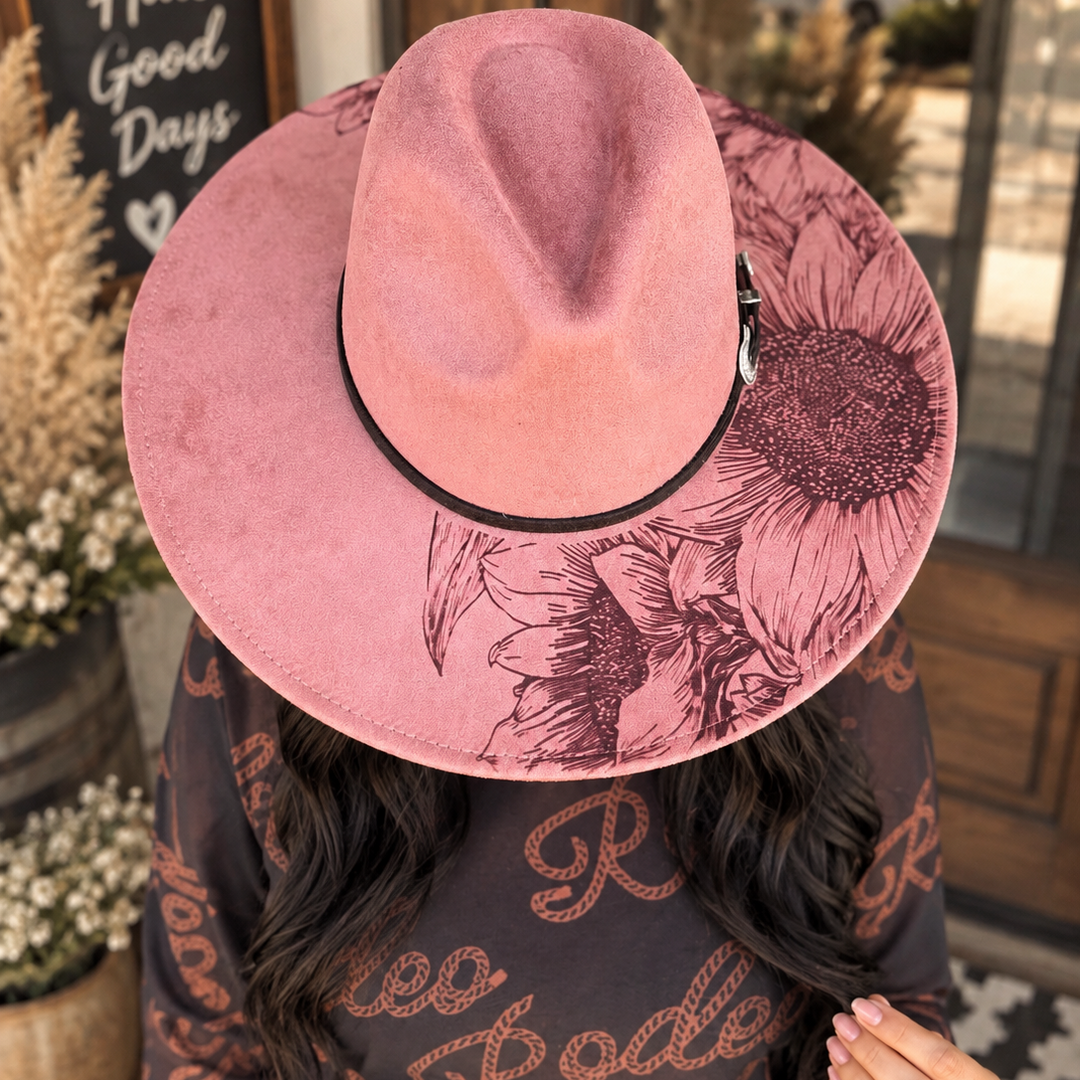 Woman wearing the Sunset Bloom dusty rose wide-brim Western hat with dark sunflower artwork