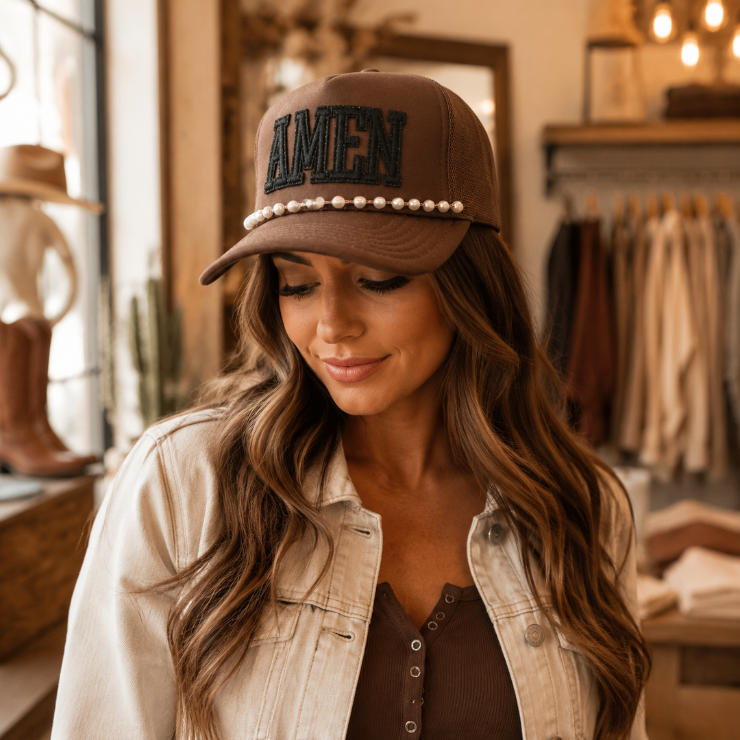 Woman wearing a brown AMEN trucker hat with black glitter patch and pearl brim chain