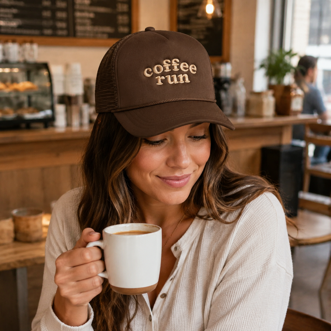 Woman wearing the Coffee Run dark brown embroidered mesh trucker hat at a cafe