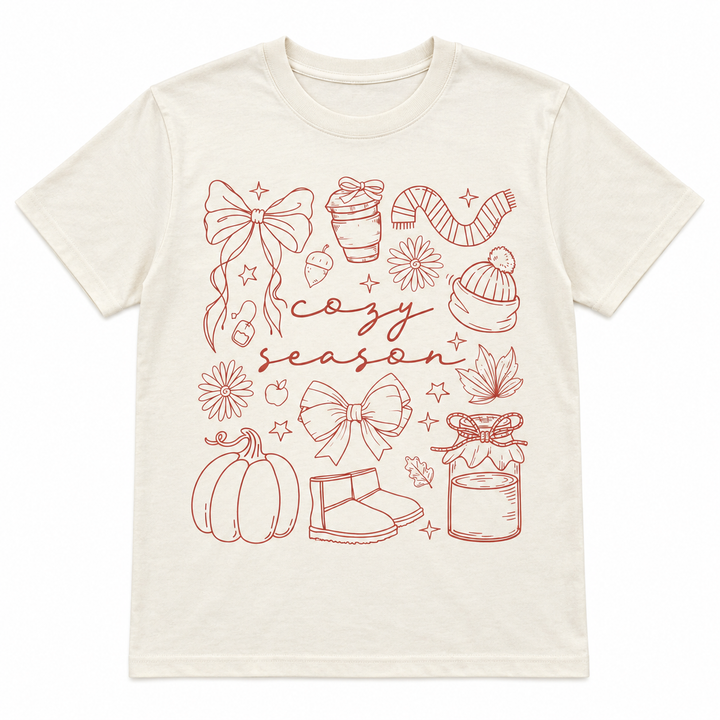 Cozy Season Essentials Natural Fall Graphic Tee laid flat on pure white
