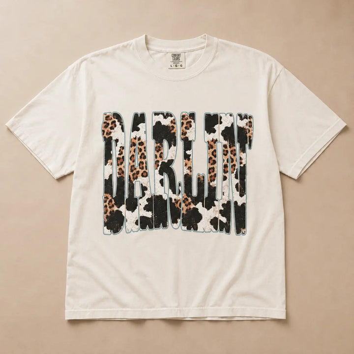 Ivory Darlin graphic tee with leopard, cow print, and turquoise details, flat product view