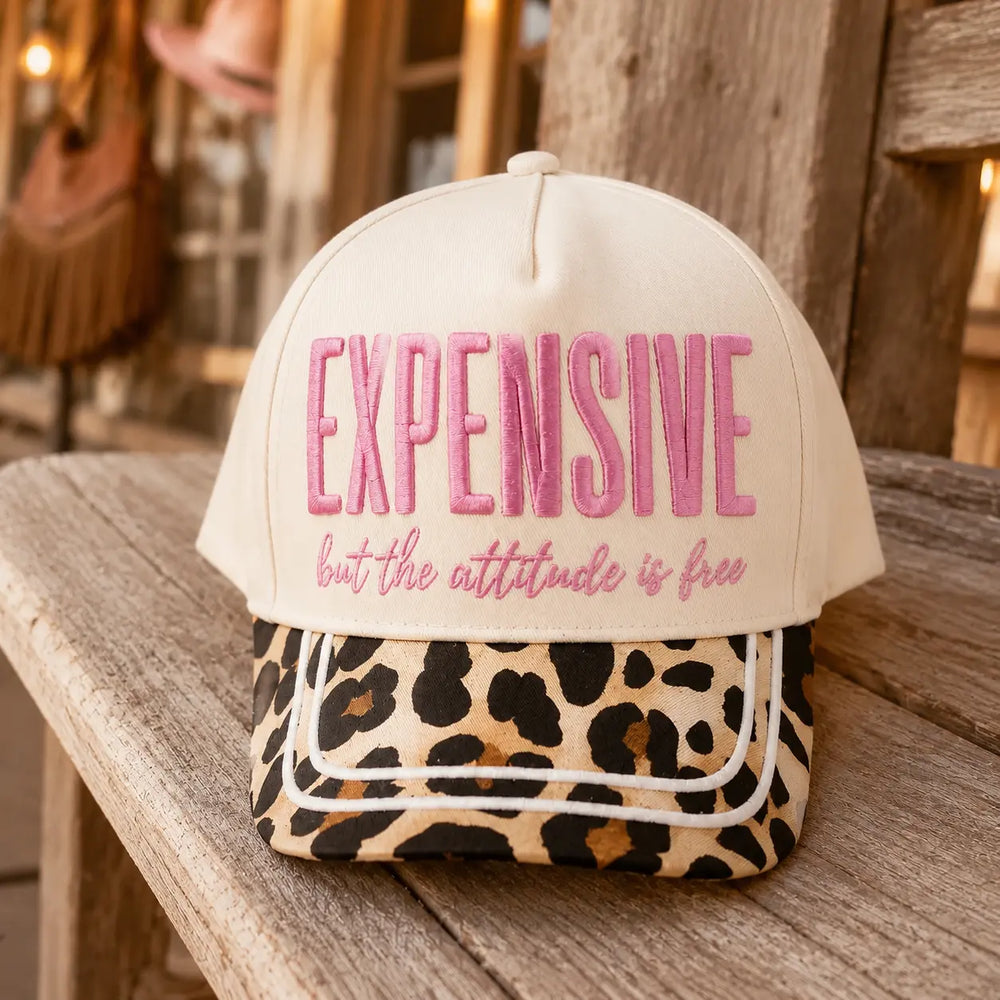 Expensive But the Attitude Is Free trucker hat on a rustic wood porch bench