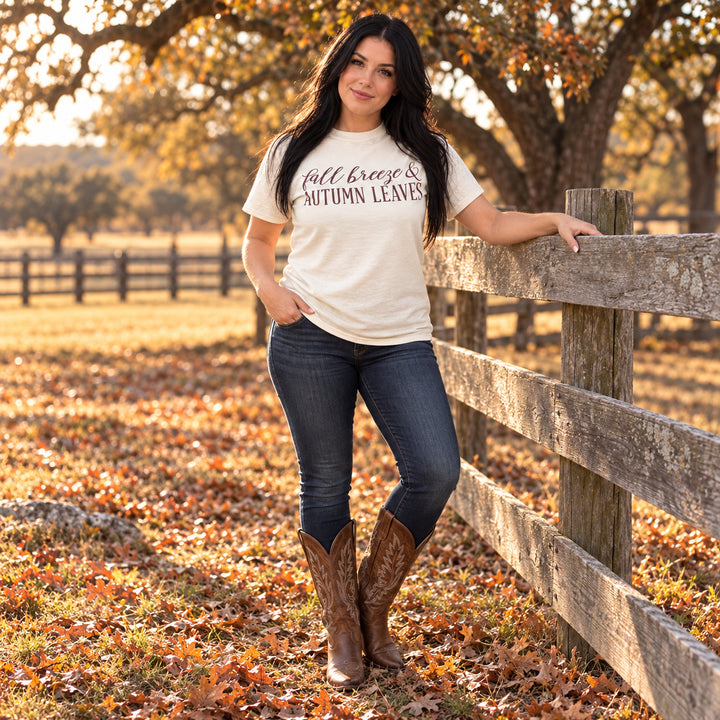 Woman wearing Fall Breeze and Autumn Leaves Natural Graphic Tee beside a Texas ranch fence