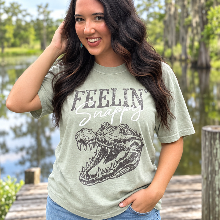 Feelin Snappy sage gator tee close model view beside a Southern pond