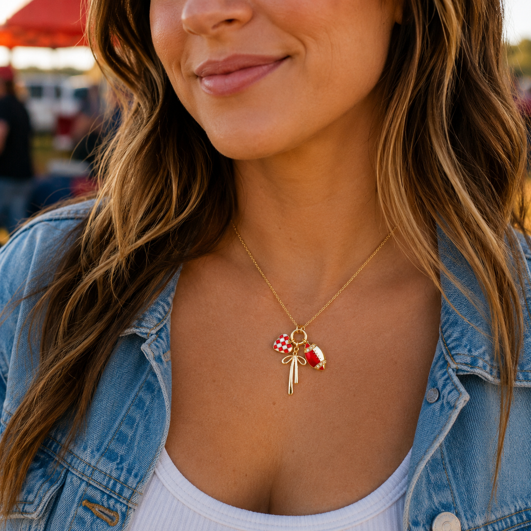 Woman wearing a delicate red football, bow, and checkered-heart charm necklace