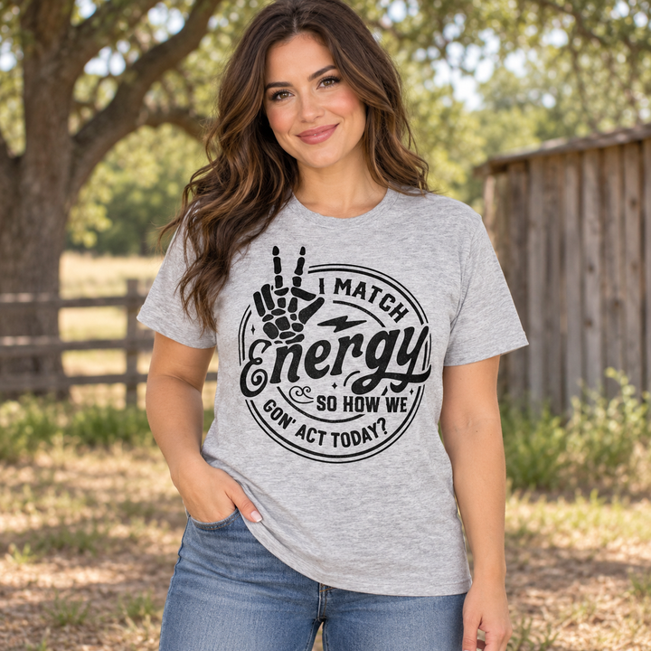 Brunette wearing the heather grey How We Gonna Act graphic tee in a close Texas ranch portrait