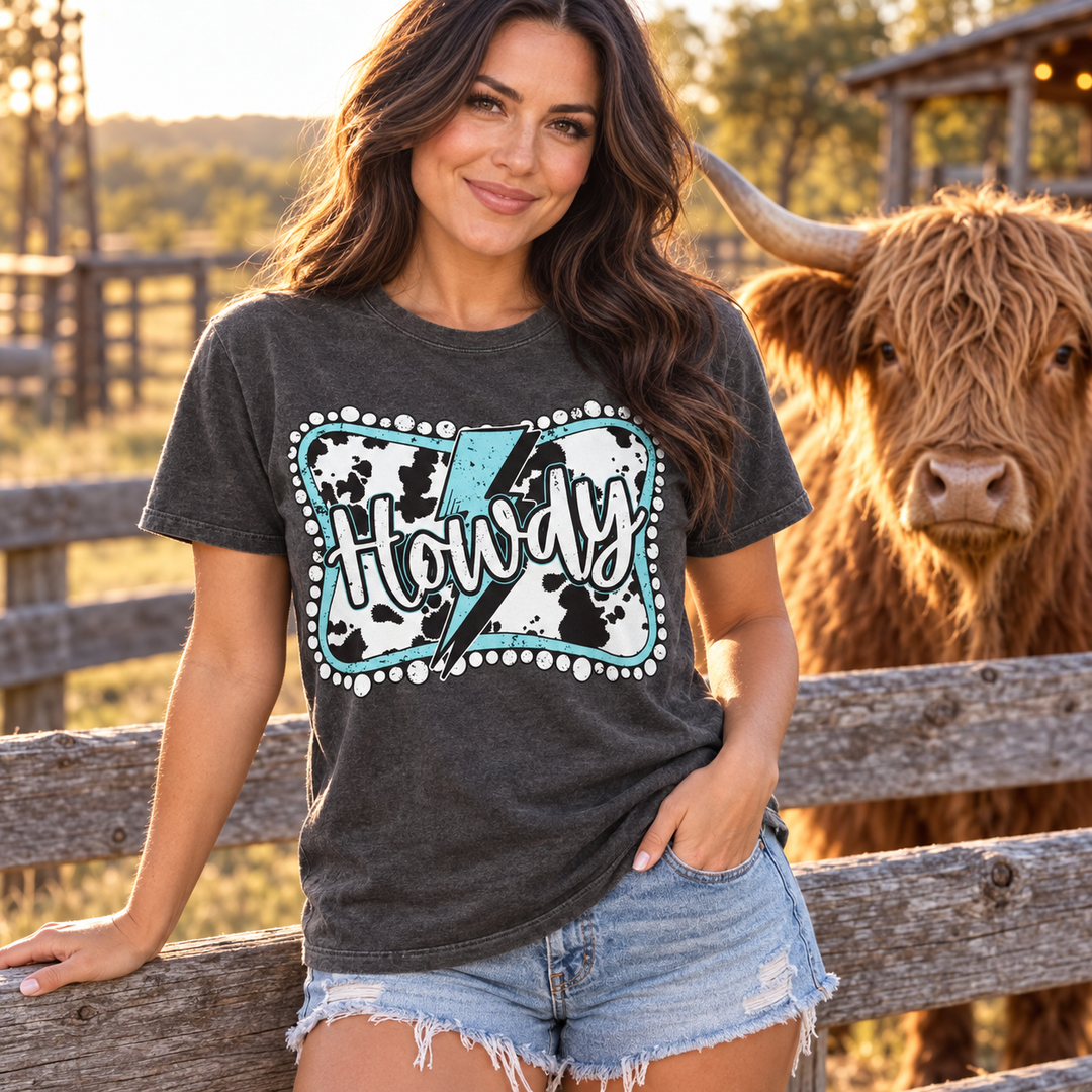 Woman wearing Howdy Cow Turquoise Lightning Pepper Graphic Tee beside a Highland cow
