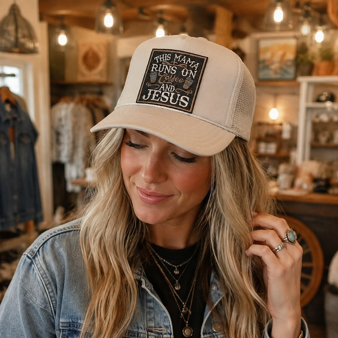 Woman wearing tan This Mama Runs on Coffee and Jesus trucker hat in a Western boutique