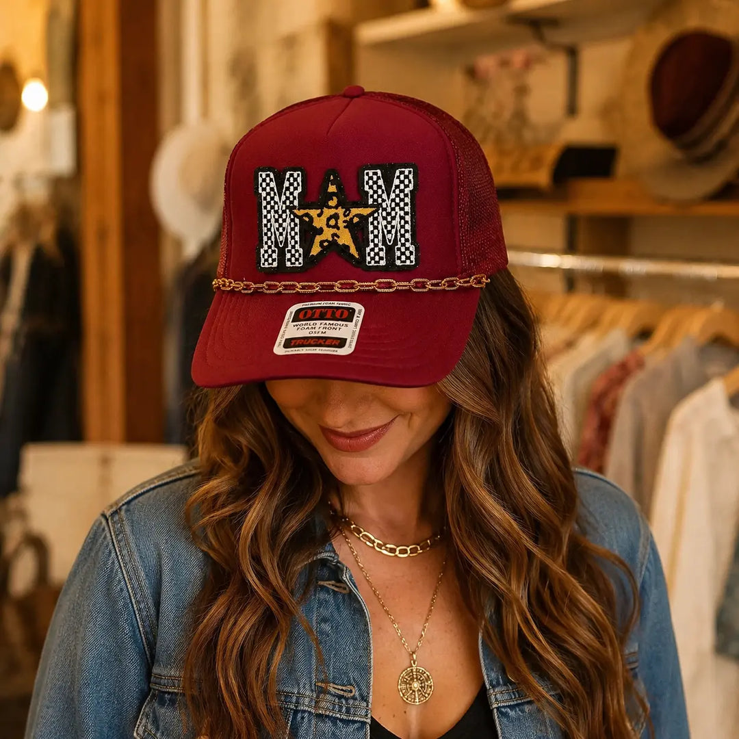 Woman wearing burgundy MOM trucker hat with checkered letters, leopard star, and gold brim chain