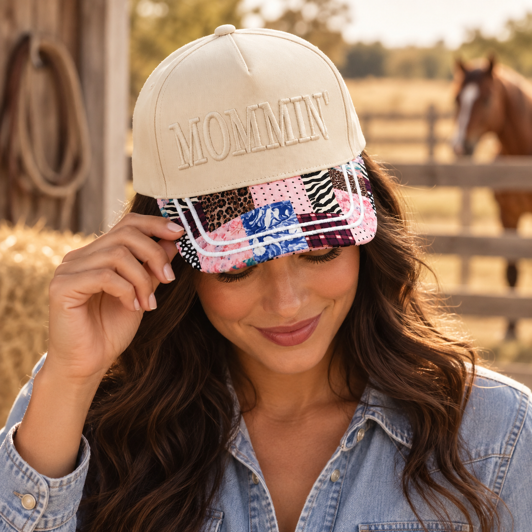 Woman wearing the Mommin embroidered faux patchwork trucker hat in a Western ranch setting