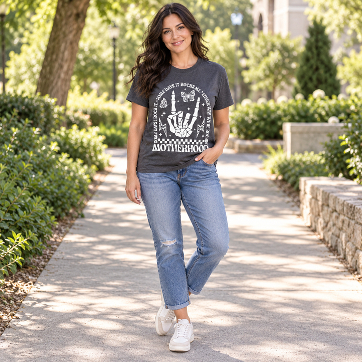 Dark-haired model wearing Motherhood Rocks charcoal graphic tee outdoors