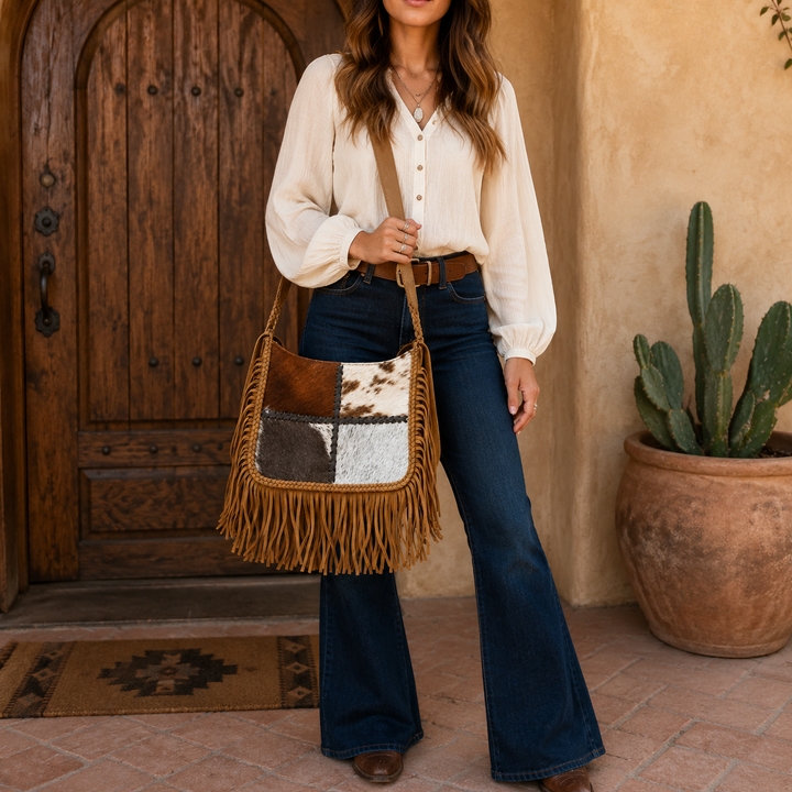 Woman carrying the Outlaw Luxe cowhide patchwork fringe shoulder bag at a Western adobe entryway