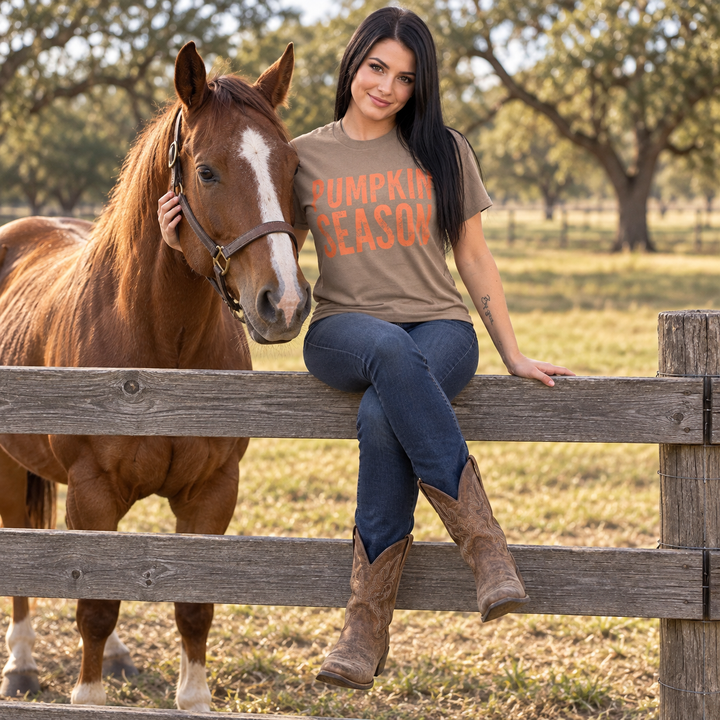 Woman wearing Pumpkin Season fall tee seated beside a horse