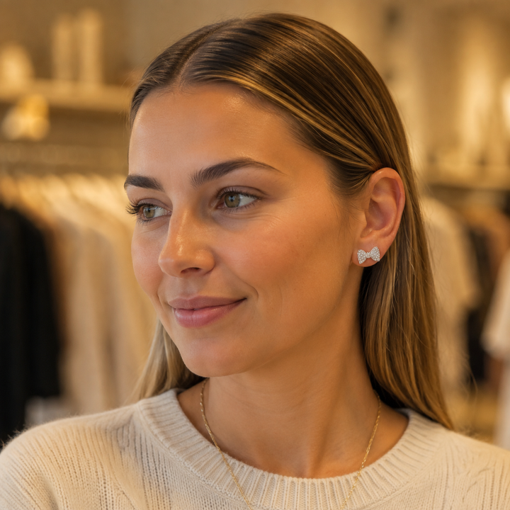 Woman wearing small silver-tone rhinestone bow stud earrings in a boutique