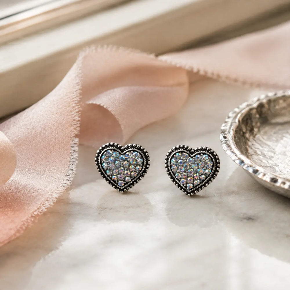 Rhinestone heart stud earrings styled with a blush ribbon on a softly lit vanity