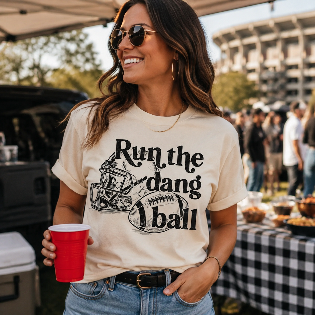 Woman wearing an ivory Run the Dang Ball football graphic tee at a tailgate