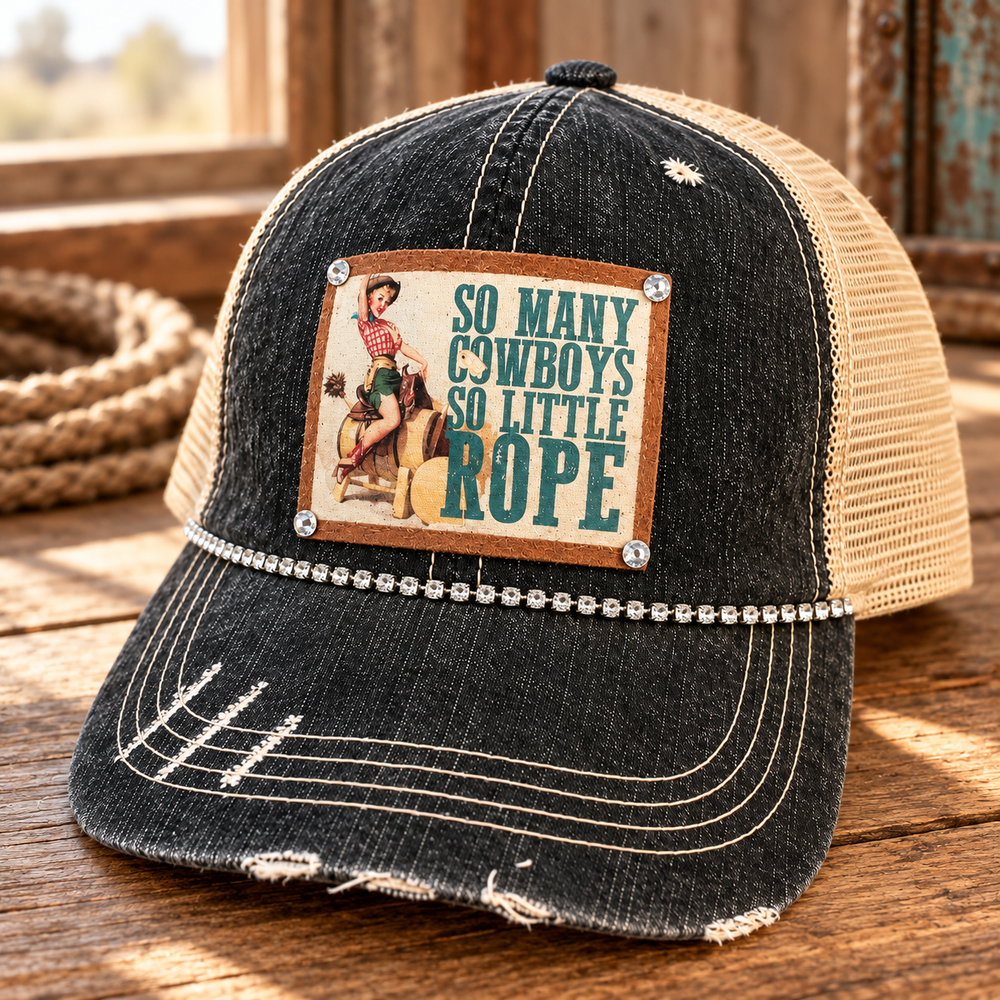 Close three-quarter view of So Many Cowboys Trucker Hat with distressed black front, tan mesh, cowgirl patch, and rhinestone trim